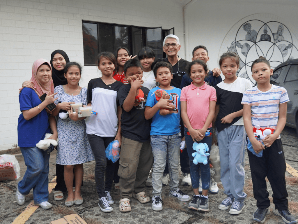 A group of Filipino children standing and smiling with Dr. Urbi