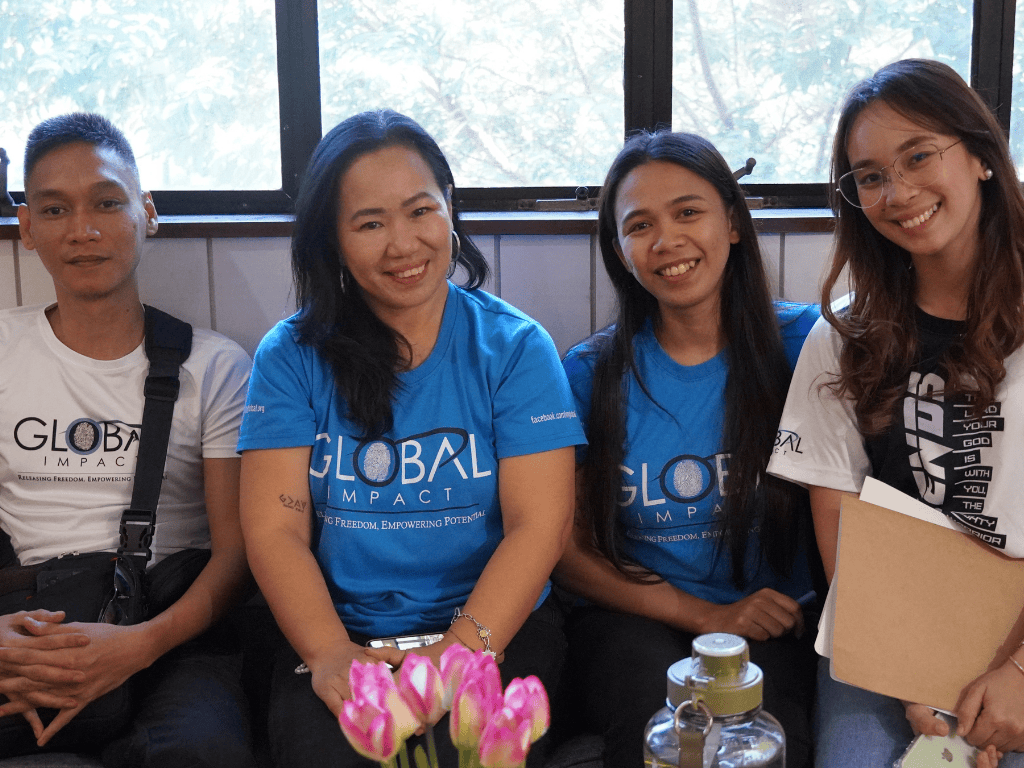 Members of the global impact team, wearing their blue-branded shirts, sitting and smiling at the camera 