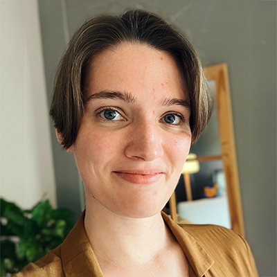 Woman with short brown hair and a yellow top slightly smiling at the camera