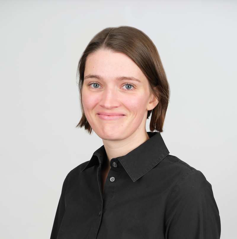 young woman with short brown hair slightly smiling, wearing a black button up 