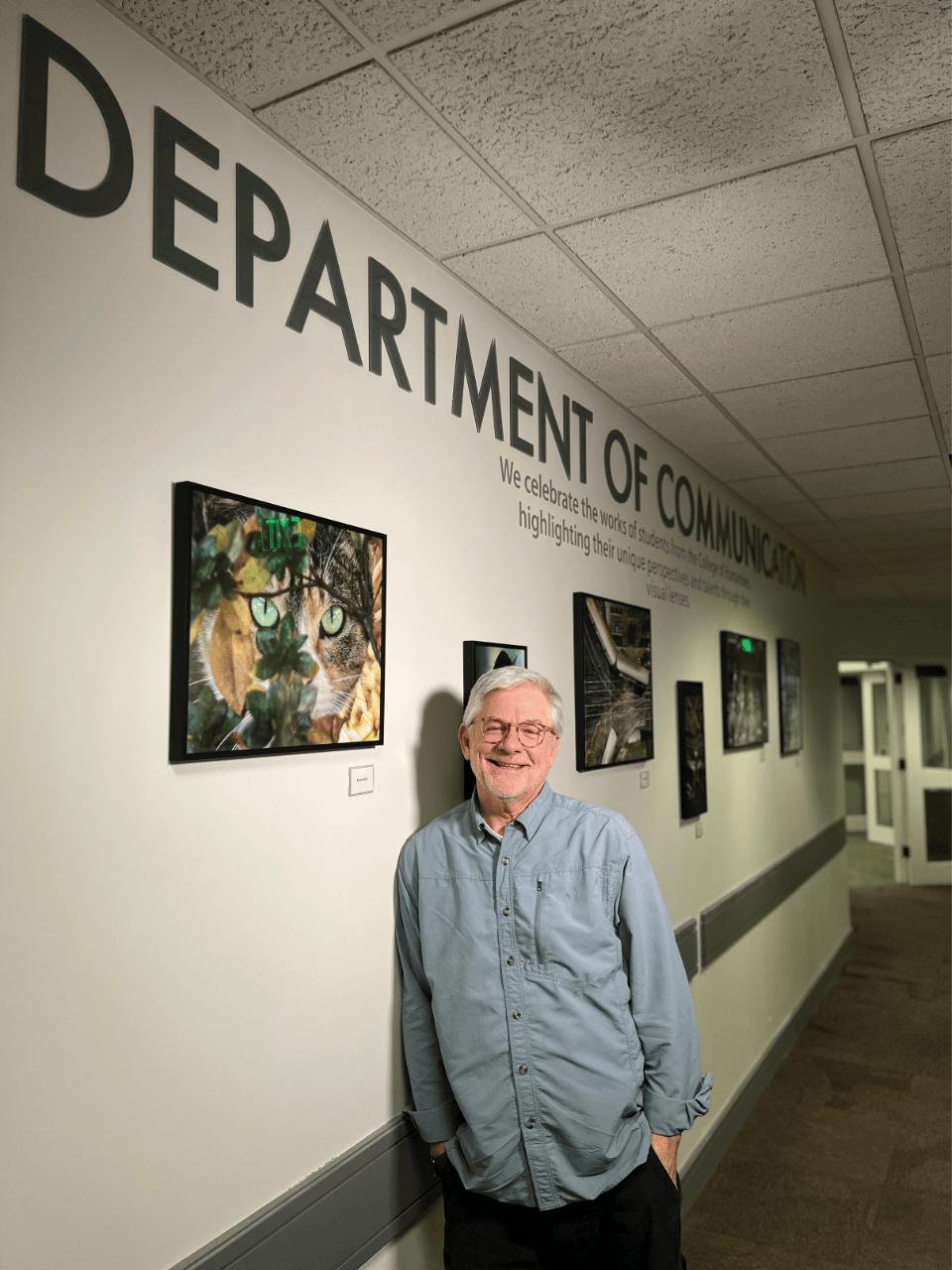 Professor Roger Tuttle, slightly smiling, leaning against the Community Connection gallery walk